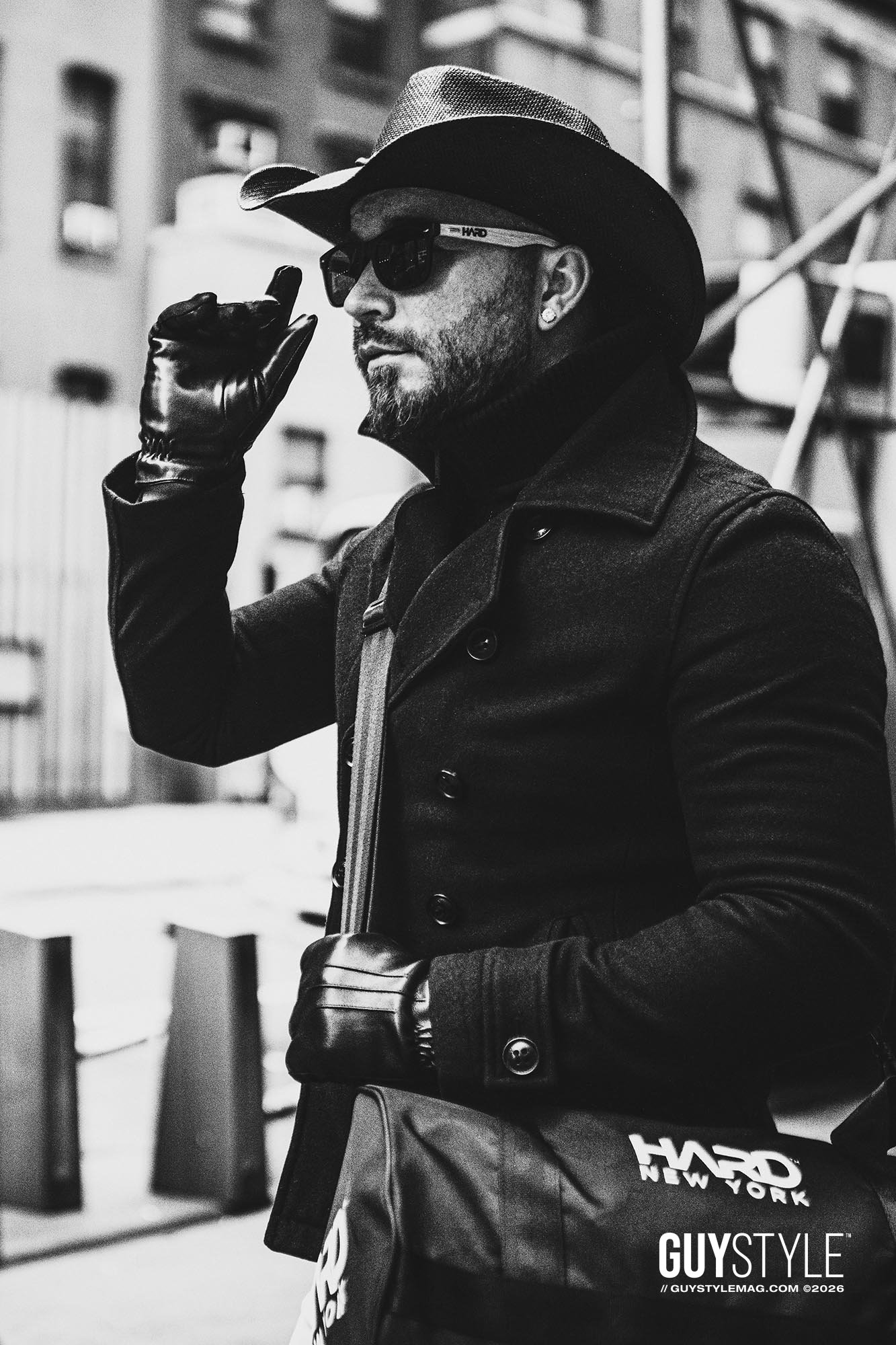 Maxwell Alexander adjusting his sunglasses in a cowboy hat, leather gloves and black coat while carrying a HARD NEW YORK bag in Manhattan.
